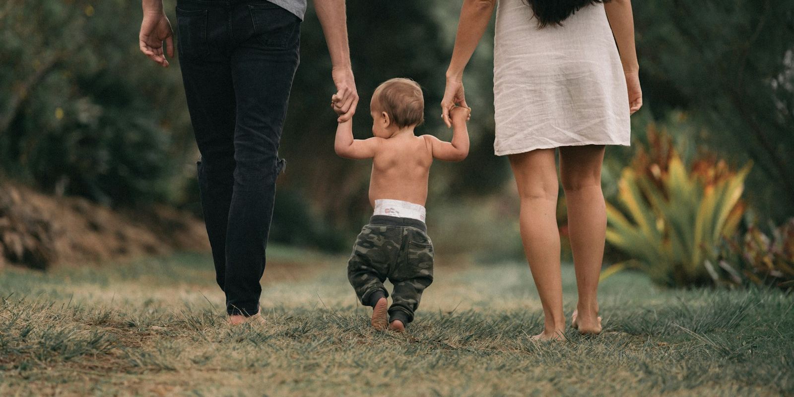 Pai e mãe de mãos dadas com o filho pequeno, caminhando na grama